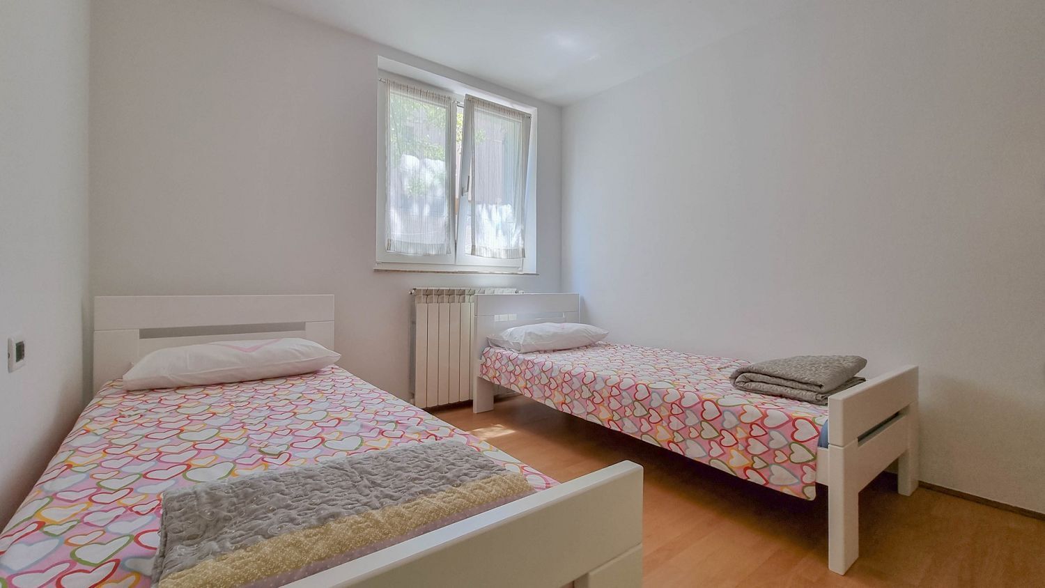 Une chambre avec deux lits, une fenêtre et un radiateur.