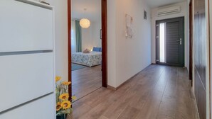 Un pasillo con una cama al fondo, un armario blanco y una puerta que da a otra habitación.