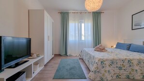 Un dormitorio con cama, televisor, armario y ventana con cortinas.