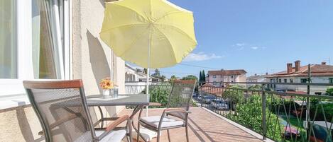 A balcony with a table and chairs, a yellow umbrella, and a view of the neighborhood.