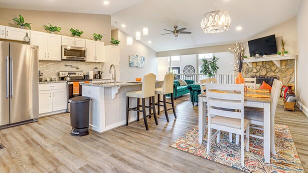A modern kitchen with stainless steel appliances, a central island with bar stools, and a dining area with a stone fireplace. - Cozy Country Livin! Gem 17 Mi to Lakepoint Sports (Woodstock)