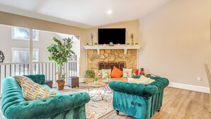 A living room with two teal velvet sofas, a stone fireplace, and a flat-screen TV mounted above it. - Cozy Country Livin! Gem 17 Mi to Lakepoint Sports (Woodstock)