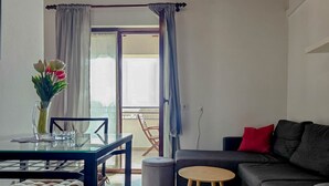 A living room with a sofa, a dining table with chairs, a small round table, and a vase with flowers. - Mediterranean apartment only 700 meters to the beach with sea view, barbecue, private parking (Novigrad)