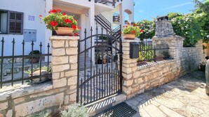 A two-story building with a stone wall and metal gate. There are flower pots on the wall and a sign above the gate. - Mediterranean apartment only 700 meters to the beach with sea view, barbecue, private parking (Novigrad)