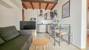 A compact living space with a sofa, a TV, a small dining table, and a kitchen area with a stove and cabinets. - Mediterranean apartment only 700 meters to the beach with sea view, barbecue, private parking (Novigrad)