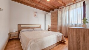 A bedroom with a wooden bed, a nightstand, a wardrobe, and a window with curtains. - Mediterranean apartment only 700 meters to the beach with sea view, barbecue, private parking (Novigrad)