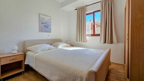 Ein Schlafzimmer mit einem Bett, einem Nachttisch, einem Fenster mit Vorhängen und einem Bild an der Wand.