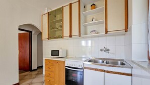 Une cuisine de taille réduite, avec des meubles blancs, un four à micro-ondes, un four traditionnel et un évier.