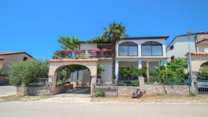 Une maison à deux étages dotée d’un balcon, d’une arche en pierre et d’un petit jardin.