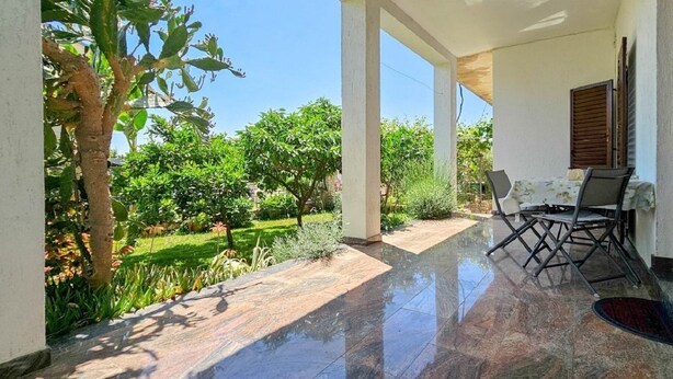 Un espace extérieur abrité, doté d’une table et de chaises, entouré de verdure et surplombé par un ciel dégagé.