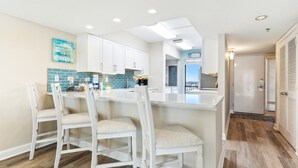 Una cocina moderna con muebles blancos, un salpicadero azul y una isla central con taburetes de bar.