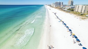 Une plage aux eaux turquoise et limpides, une longue étendue de sable blanc et une rangée de parasols.
