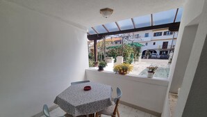 A small balcony with a table and two chairs, a potted plant, and a view of buildings and a street.