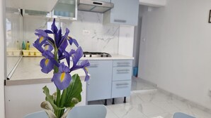 A modern kitchen with light blue cabinets, a white countertop, and a vase with purple flowers on a table.