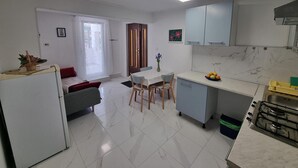 A compact kitchen with a dining area, a refrigerator, a stove, and a window with curtains.