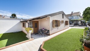 Ein zweistöckiges Haus mit Terrasse, einem kleinen Tisch und Stühlen sowie einem gepflegten Rasen.