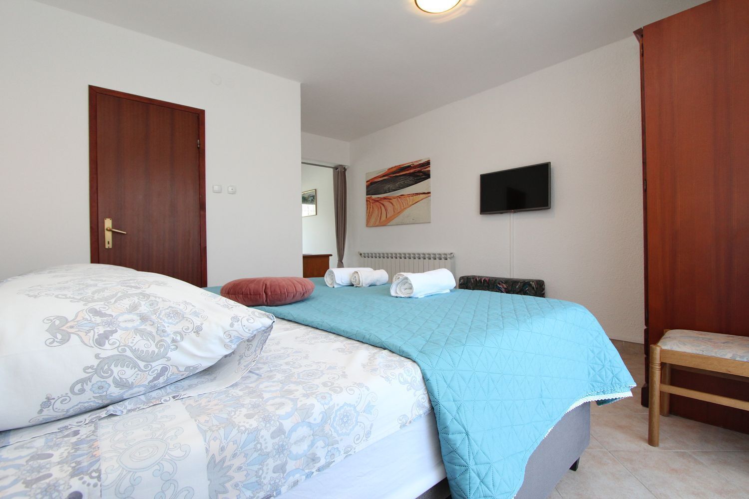 A bedroom with a bed, a chair, a television, and a painting on the wall.