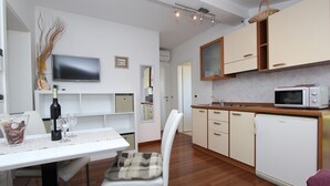 Un espace de vie compact comprenant un coin repas, une kitchenette et un téléviseur fixé au mur.