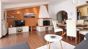 A modern living room with a fireplace, a dining area, and a kitchen visible through an archway.