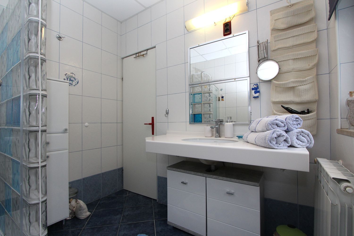 A bathroom with a white sink, mirror, and towel rack. There is a shower area with a glass door and a toilet.