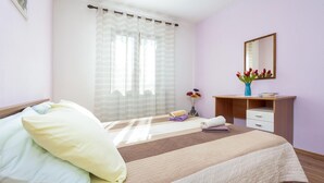 Ein ordentlich bezogenes Bett mit Kissen, ein Nachttisch mit Blumenvase und ein Spiegel an der Wand.