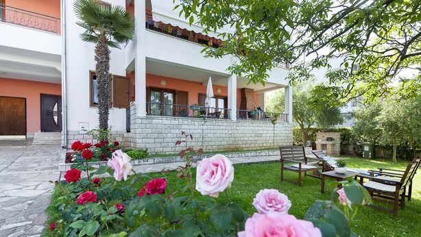 Ein zweistöckiges Gebäude mit einer Steinaußenfassade, einem Balkon mit Gartenmöbeln und einem Rosengarten.