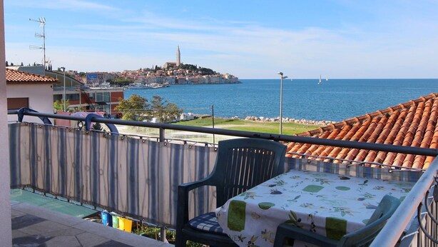 Un balcón con vistas al mar, una silla y una mesa con mantel.