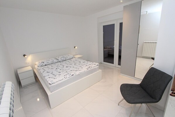 A modern bedroom with a large bed, a chair, a nightstand, and a sliding glass door leading to a balcony. - Modern flat right by the sea and only 400 metres to the beach - in Rovinj (Rovinj)