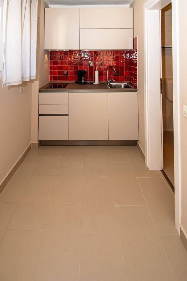 A compact kitchen with white cabinets, a red tiled backsplash, and a stainless steel sink. - Stunning flat right on the blue, crystal-clear Adriatic Sea in Rovinj (Rovinj)