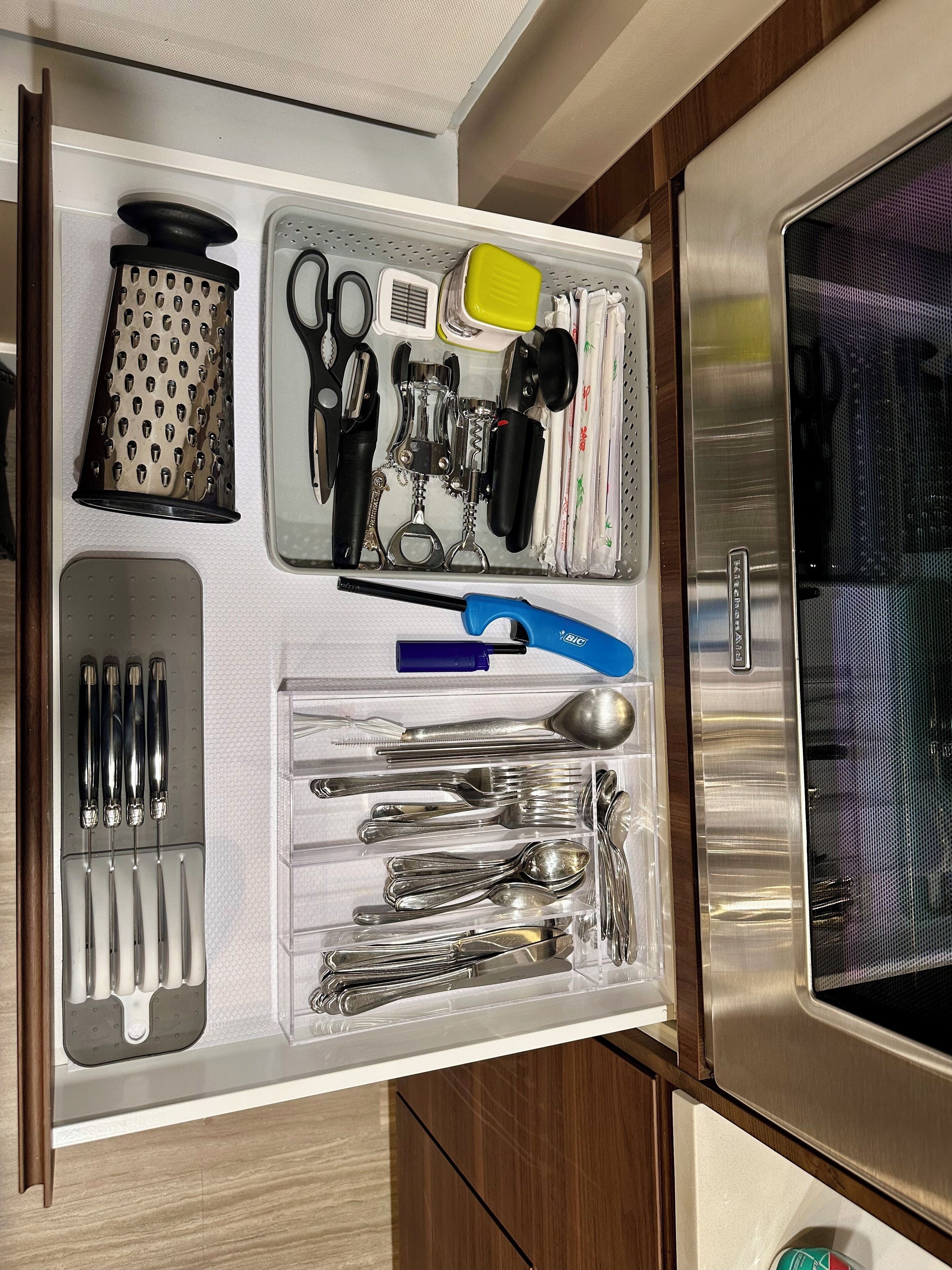Un cajón de cocina con utensilios, un rallador, un abrelatas y un microondas.