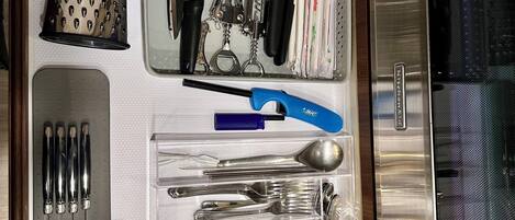Un cajón de cocina con utensilios, un rallador, un abrelatas y un microondas.