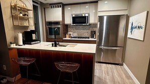 A modern kitchen with a central island, stainless steel appliances, and a herringbone-patterned backsplash. - Century park Condo Oasis (Edmonton)