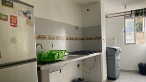 Eine kleine Küche mit Kühlschrank, Gasherd und Spüle. Auf der Arbeitsfläche stehen Plastikbehälter und ein Topf.