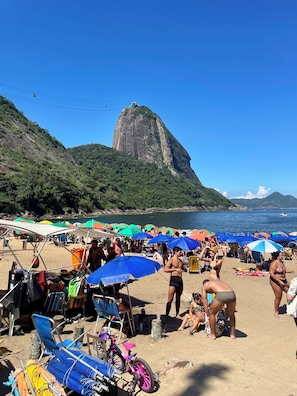 A beach with people, umbrellas, and a prominent mountain in the background.