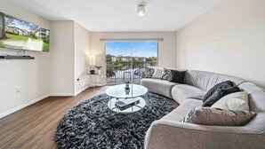 En moderne stue med en grå sofa, et rundt sofabord og en sort, lurvet måtte.