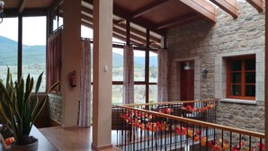 A spacious balcony with a stone wall, wooden beams, and a view of the countryside.