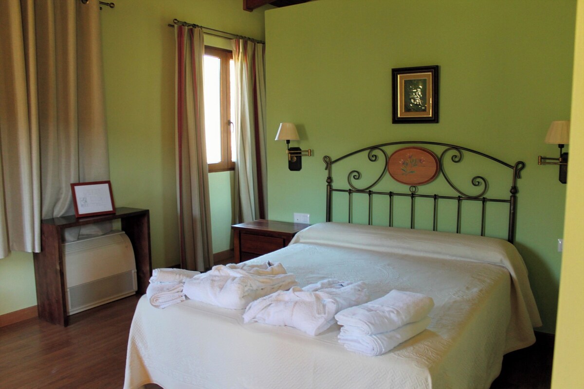 A hotel room with a bed, a bedside table, a lamp, and a window with curtains.