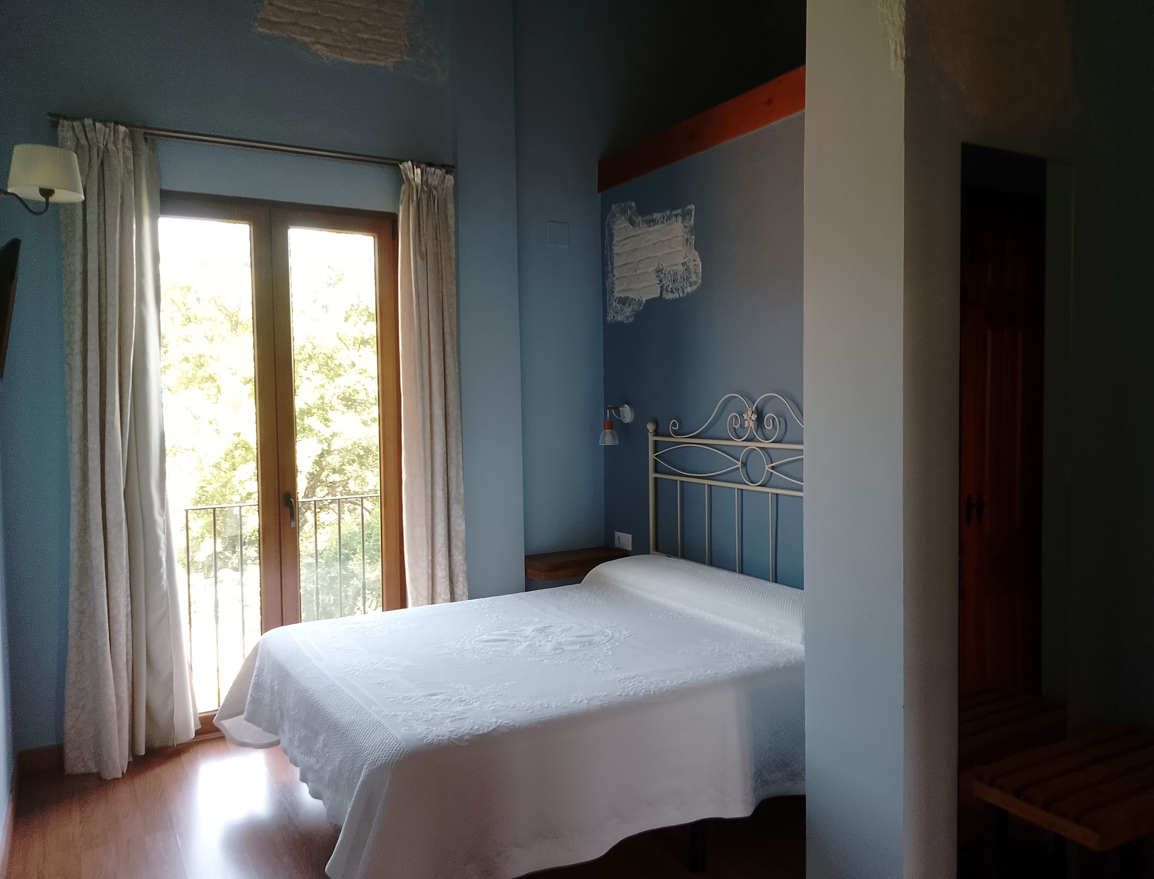 A bedroom with a bed, a window with curtains, a wall with a decorative element, and a staircase.