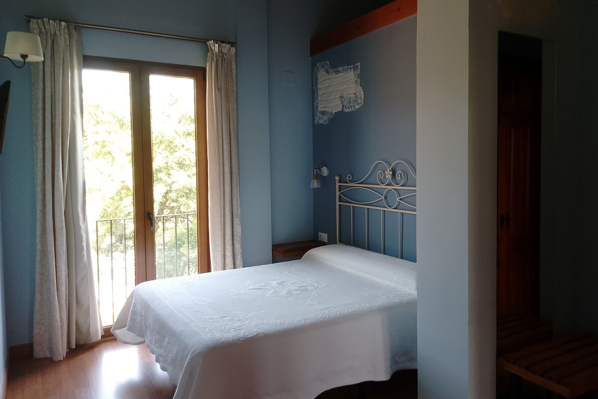 A bedroom with a bed, a window with curtains, a wall with a decorative element, and a staircase.