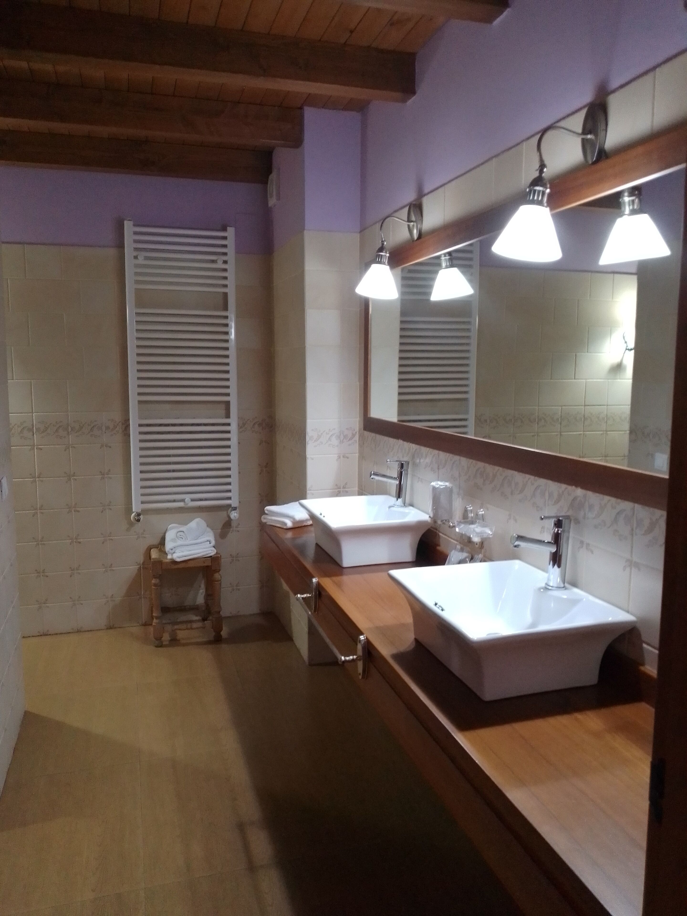 Un baño con dos lavamanos, un mueble de tocador de madera, un taburete pequeño y una ventana con persianas.