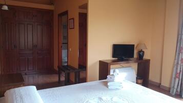 A hotel room with a bed, a television on a wooden stand, a table with a lamp, and a wardrobe.