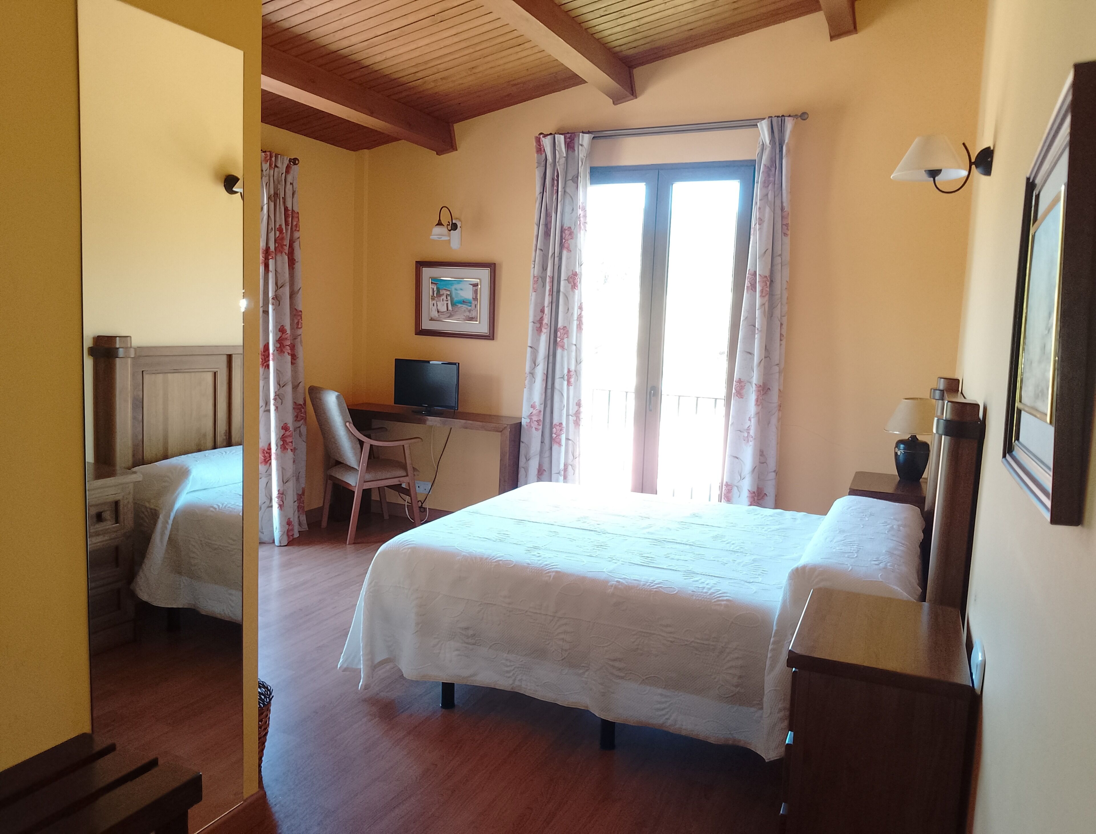 Habitación de hotel con dos camas, un escritorio con computadora, una silla, un televisor y un cuadro en la pared.