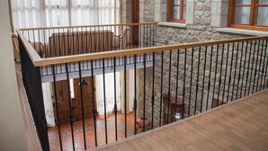A stone building with a wooden balcony railing, a tiled floor, and a window with a wooden frame.