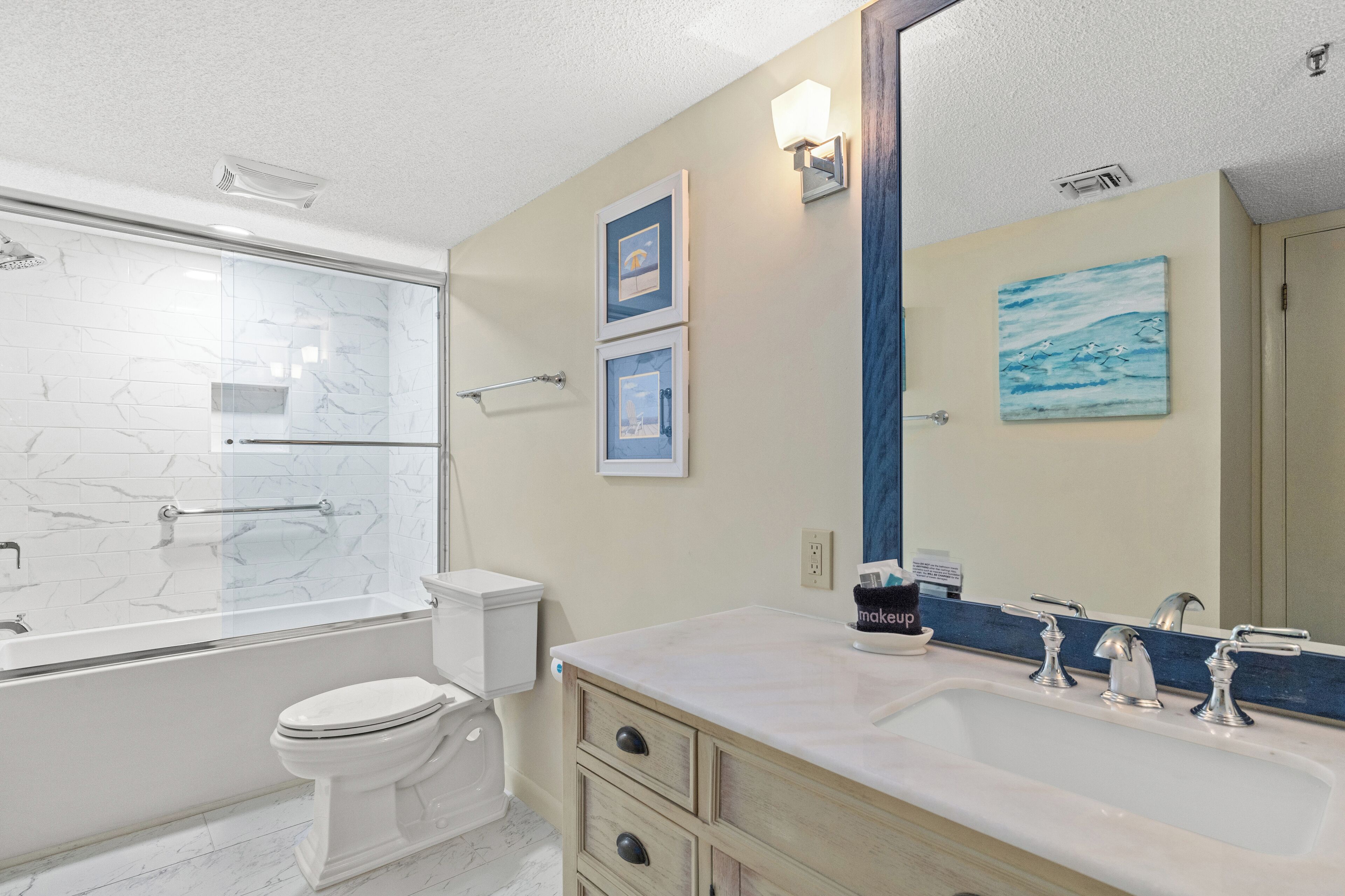 A bathroom with a glass-enclosed shower, a toilet, a sink with two faucets, and a mirror.