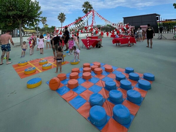 Un parque infantil con colchonetas de colores y obstáculos circulares, rodeado de una decoración festiva con banderas y mesas.
