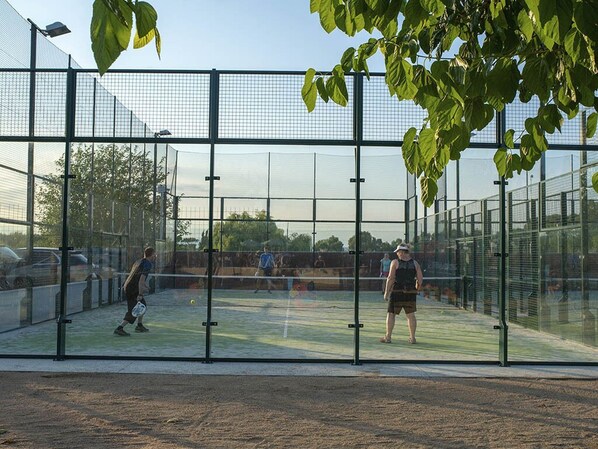 Una cancha de tenis rodeada por una valla de vidrio que permite una vista clara del entorno.