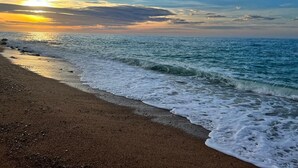 A beach with waves gently lapping onto the shore under a sunset sky.