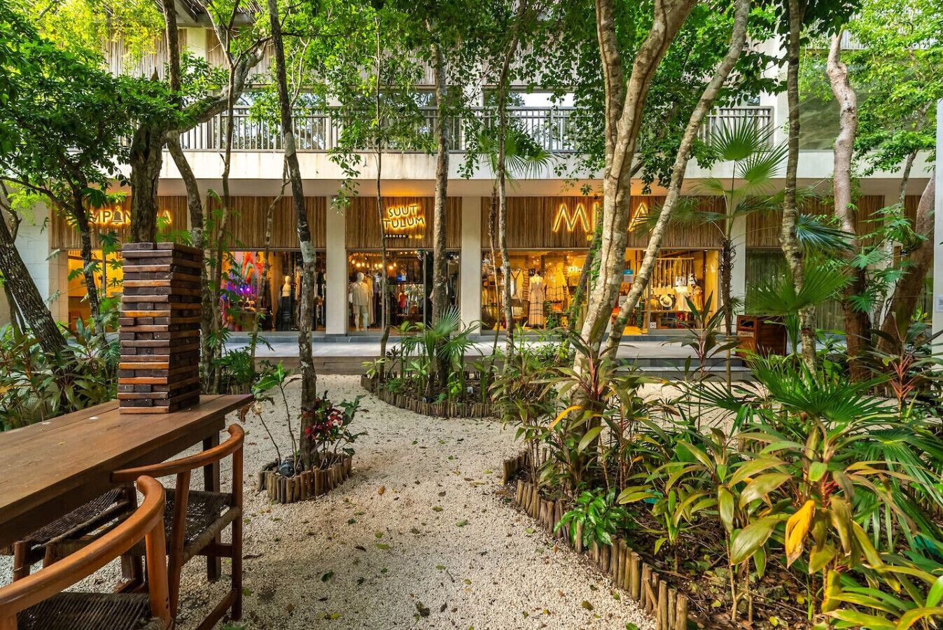 A courtyard with a wooden bench, a stack of wooden blocks, and various tropical plants.