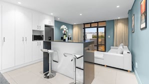 Una cocina moderna con armarios blancos, una isla central con taburetes y electrodomésticos como microondas y refrigerador.