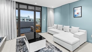 Una sala de estar moderna con un sofá blanco, una mesa de centro de vidrio y vistas a una zona residencial a través de amplios ventanales correderas.